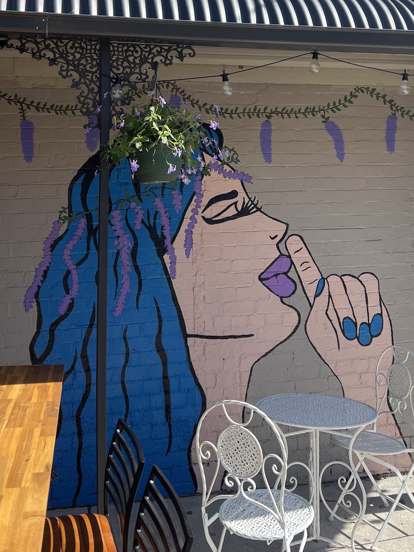 The cafe courtyard with its hand-painted wisteria mural, white bistro tables and festoon lights