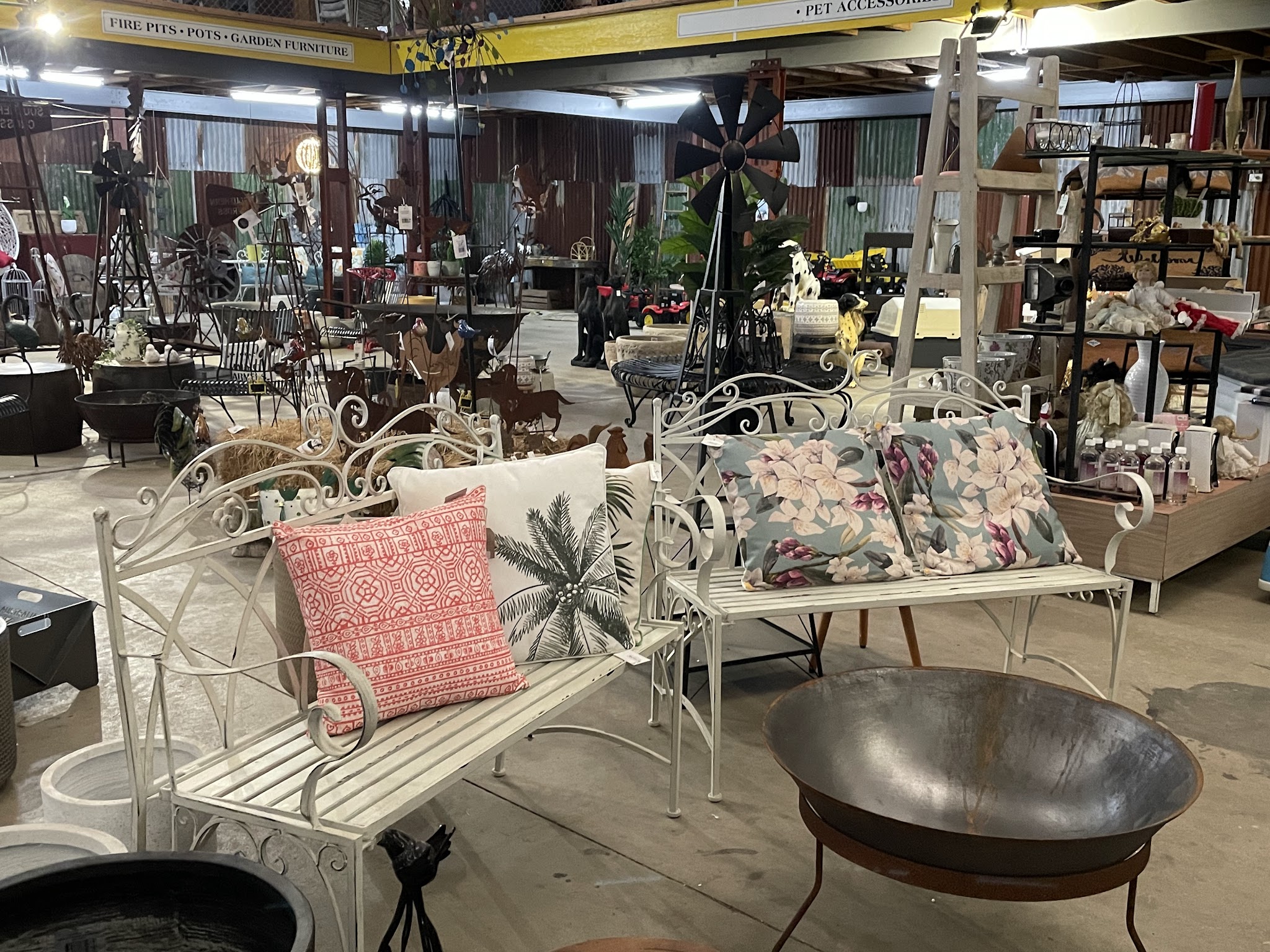 White wrought-iron benches with cushions, fire-pit bowls and metal windmills under the covered market shed