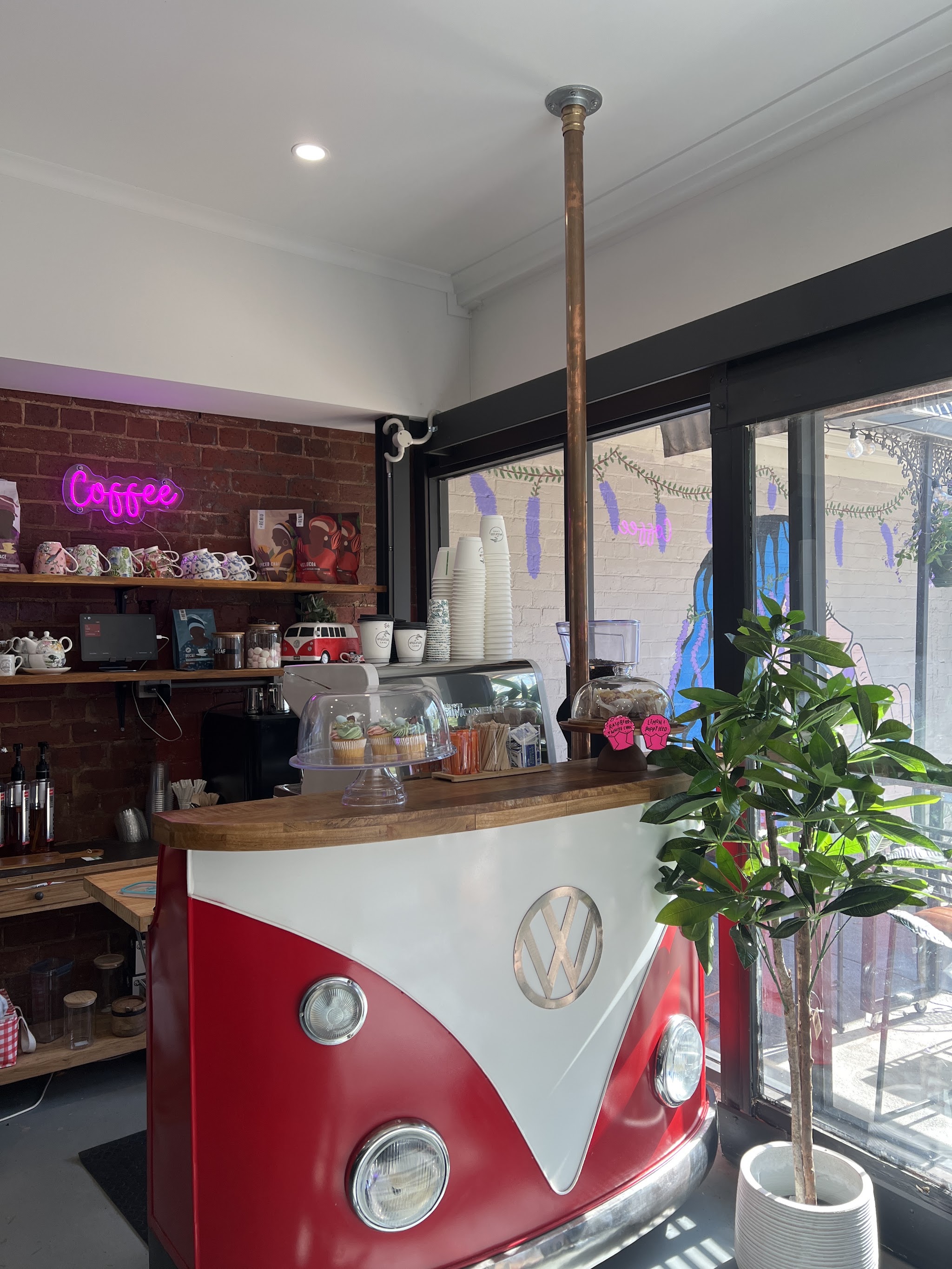 The Wisteria Lane coffee counter, built from the front half of a red and white VW Kombi, with a neon coffee sign and cupcakes under a glass dome