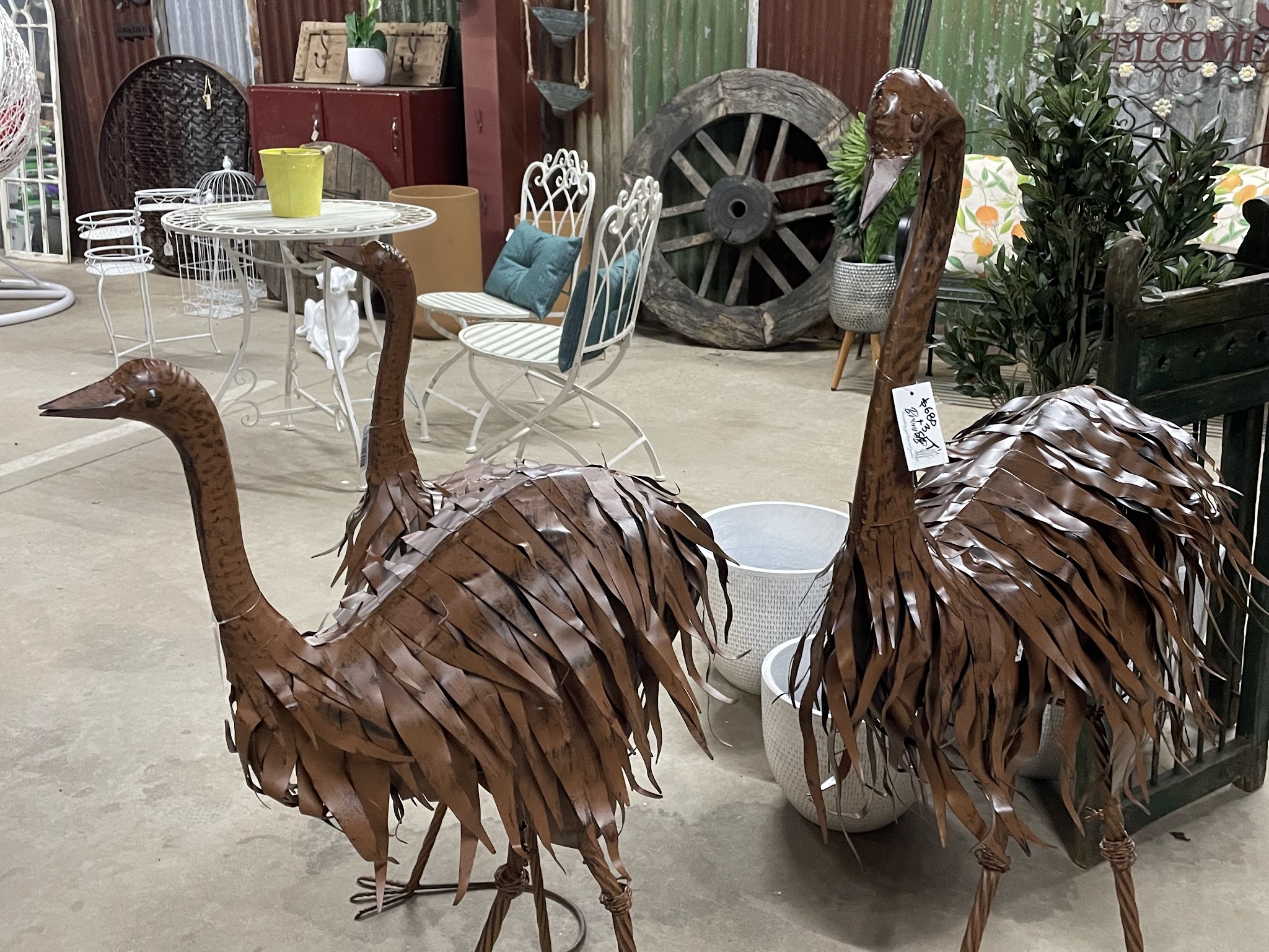 Rusted metal emu garden sculptures beside a wagon wheel and a white iron outdoor setting